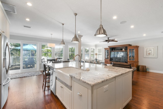 kitchen featuring dark wood-type flooring, ornamental molding, white cabinets, and a center island with sink