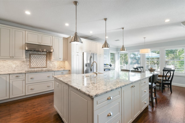 kitchen with stainless steel fridge with ice dispenser, pendant lighting, ornamental molding, a center island with sink, and dark wood-type flooring