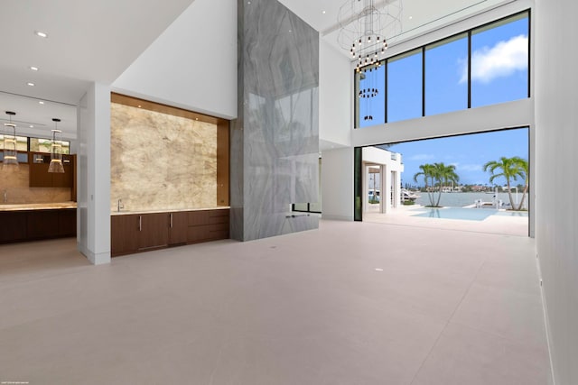 unfurnished living room featuring concrete floors, a notable chandelier, and a high ceiling