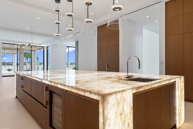 kitchen with sink, a large island, decorative light fixtures, beverage cooler, and light stone counters