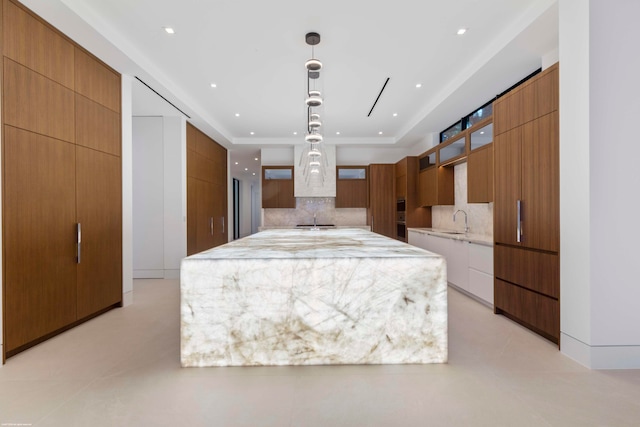 kitchen featuring oven, decorative backsplash, a spacious island, light stone countertops, and decorative light fixtures