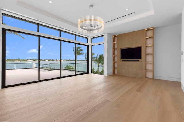 unfurnished living room featuring light hardwood / wood-style floors, a healthy amount of sunlight, a tray ceiling, and floor to ceiling windows