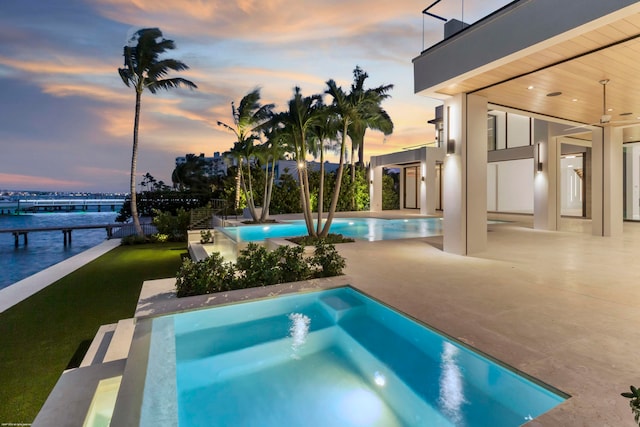 pool at dusk with a patio, a jacuzzi, a water view, and ceiling fan