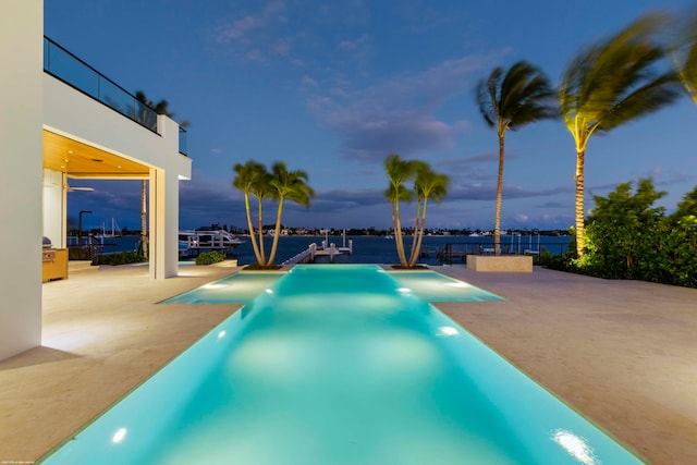 pool at dusk featuring a water view and a patio