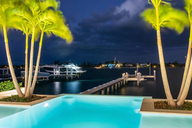 pool at night featuring a water view and a dock