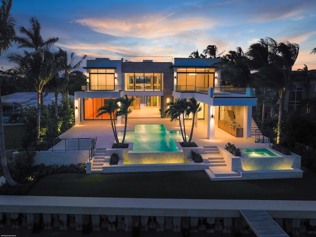 back house at dusk with a patio, an in ground hot tub, and a balcony