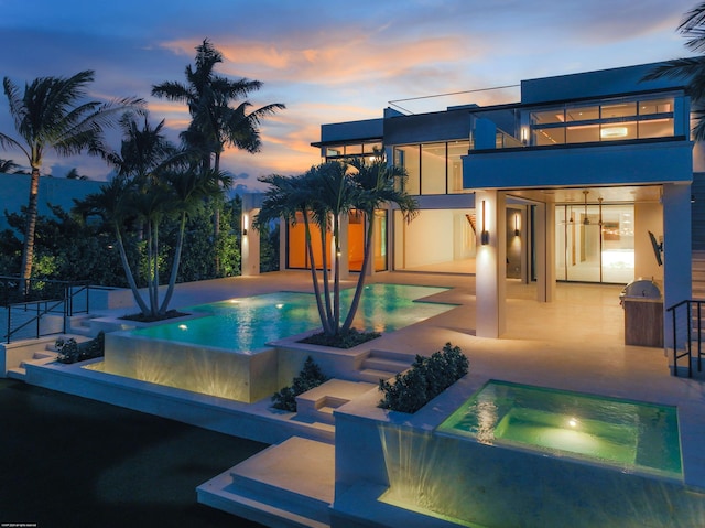 pool at dusk featuring a patio and an in ground hot tub