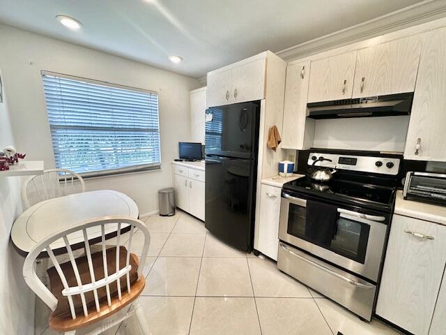 kitchen with electric range oven, black fridge, sink, light tile patterned floors, and cream cabinetry