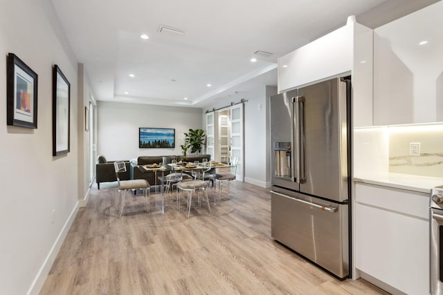 kitchen featuring a raised ceiling, light hardwood / wood-style floors, high end refrigerator, a barn door, and white cabinets