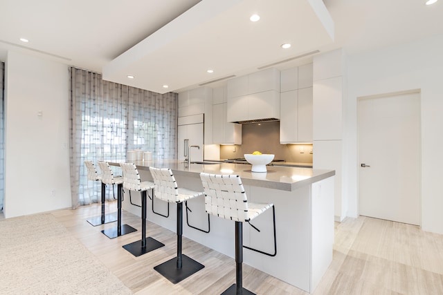 kitchen with a breakfast bar, backsplash, sink, an island with sink, and premium range hood