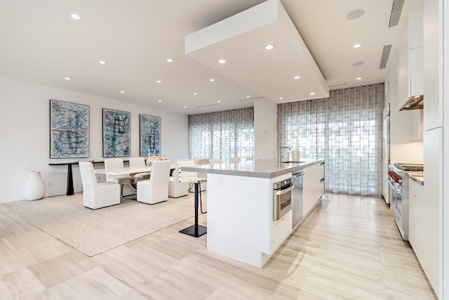 kitchen with a kitchen breakfast bar, sink, white cabinetry, stainless steel appliances, and a center island with sink