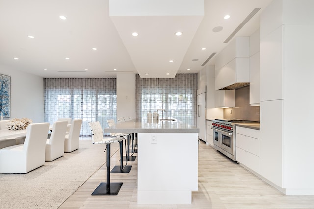 kitchen featuring a kitchen bar, high quality appliances, tasteful backsplash, a center island with sink, and white cabinets