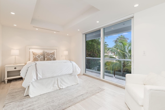 bedroom with access to outside, a raised ceiling, light wood-style flooring, and recessed lighting