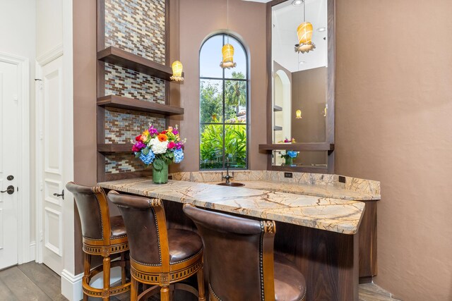 bar with hanging light fixtures, dark hardwood / wood-style flooring, backsplash, and light stone countertops