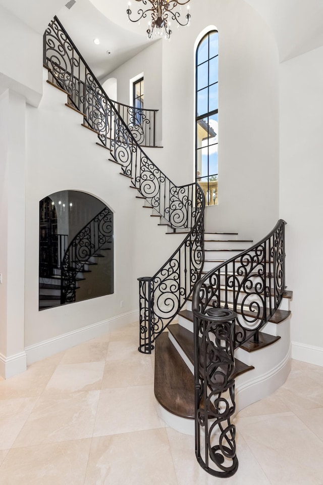 staircase with light tile flooring, a towering ceiling, and a chandelier