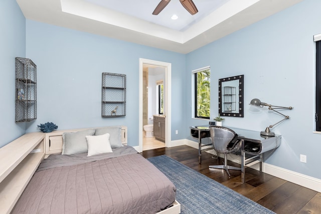 bedroom featuring ceiling fan, ensuite bathroom, a tray ceiling, and dark wood-type flooring