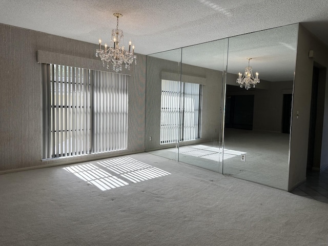 unfurnished bedroom featuring a textured ceiling, carpet flooring, and a chandelier