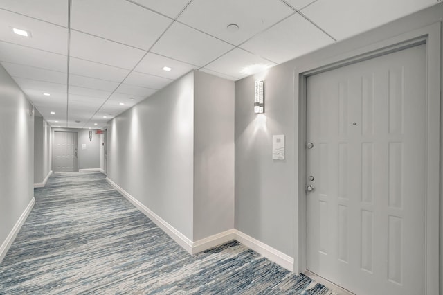 hall featuring carpet flooring and a paneled ceiling