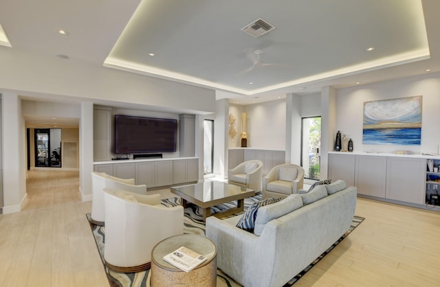 living room with ceiling fan, light hardwood / wood-style floors, and a raised ceiling