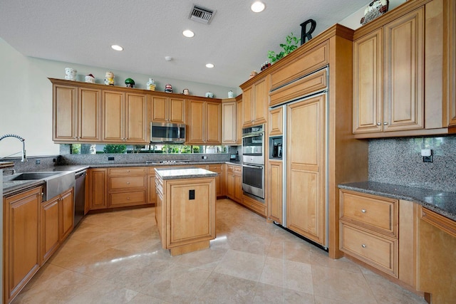 kitchen featuring sink, appliances with stainless steel finishes, a kitchen island, decorative backsplash, and dark stone counters