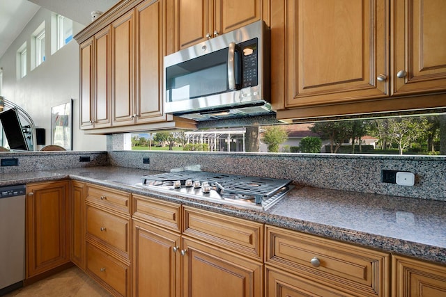 kitchen with stainless steel appliances, light tile patterned flooring, and dark stone countertops