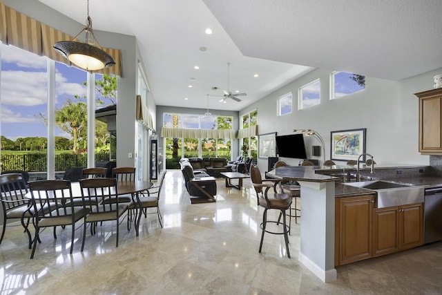 kitchen with sink, a breakfast bar area, dark stone counters, hanging light fixtures, and stainless steel dishwasher