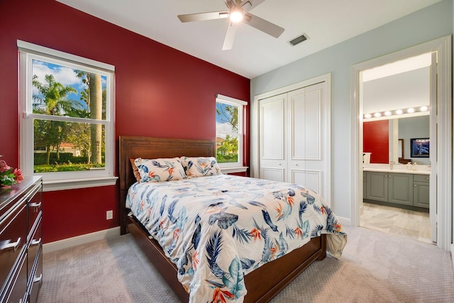 bedroom with connected bathroom, light colored carpet, a closet, and ceiling fan