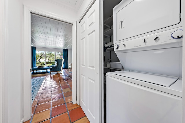 laundry area featuring stacked washer and clothes dryer, ornamental molding, and dark tile patterned flooring