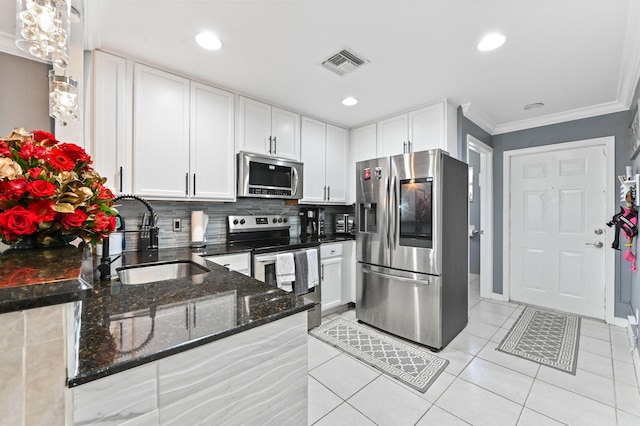 kitchen with stainless steel appliances, dark stone counters, sink, pendant lighting, and white cabinetry