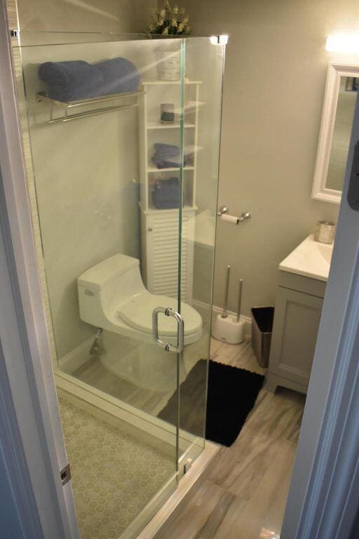 bathroom featuring hardwood / wood-style floors, vanity, toilet, and a shower with shower door