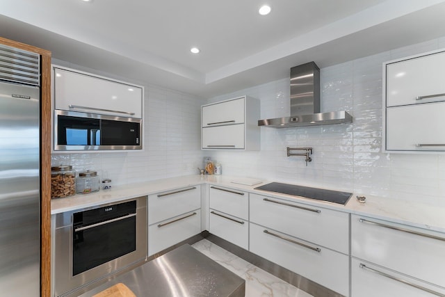 kitchen featuring wall chimney exhaust hood, white cabinetry, stainless steel appliances, and tasteful backsplash