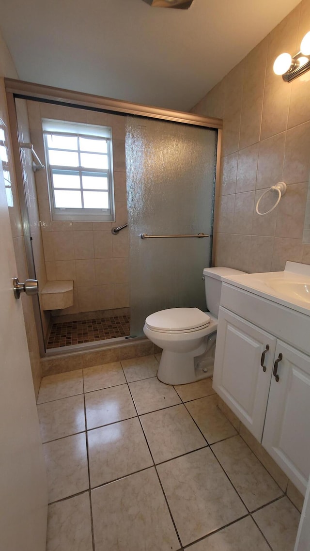 bathroom featuring tile patterned floors, toilet, a shower with shower door, and tile walls