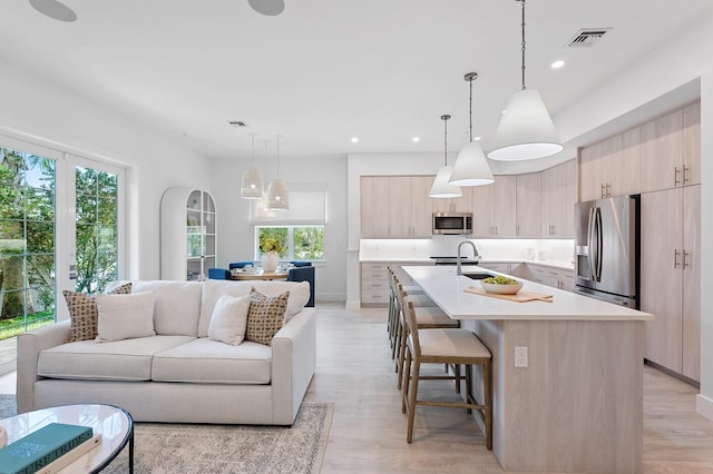 kitchen with a center island with sink, plenty of natural light, light wood-type flooring, and appliances with stainless steel finishes