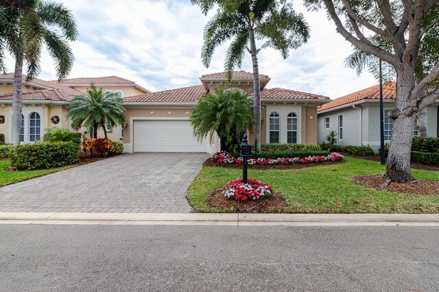 mediterranean / spanish home featuring a garage, a tiled roof, decorative driveway, and stucco siding