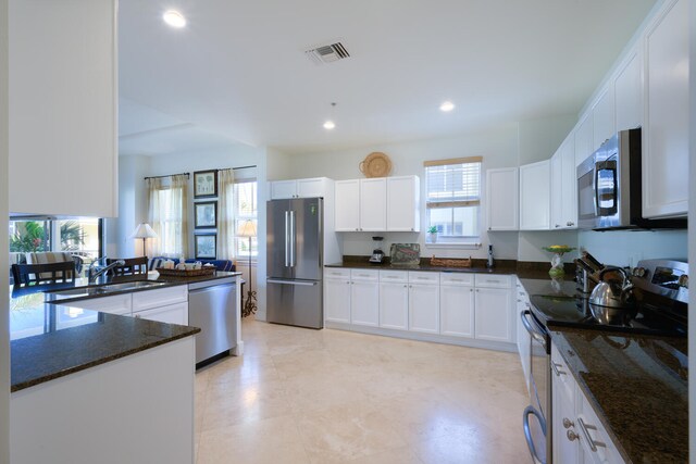 kitchen featuring stainless steel appliances, dark stone counters, white cabinets, and sink