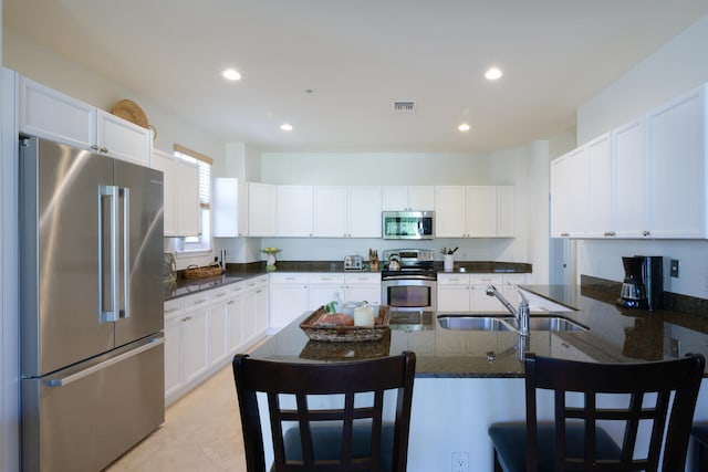 kitchen featuring a breakfast bar area, dark stone countertops, sink, white cabinets, and appliances with stainless steel finishes