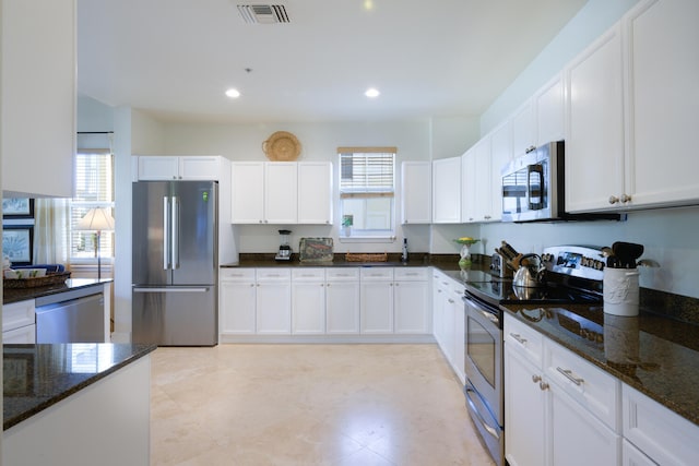 kitchen with dark stone countertops, stainless steel appliances, white cabinetry, and a healthy amount of sunlight