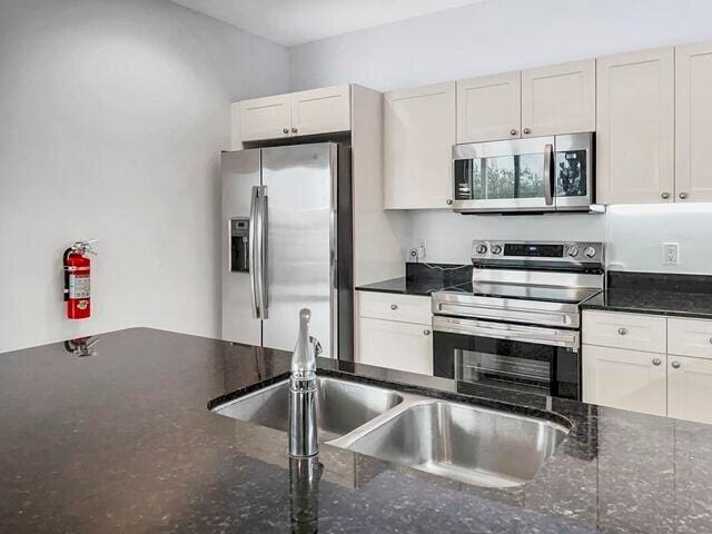 kitchen featuring appliances with stainless steel finishes, white cabinetry, a sink, and dark stone countertops