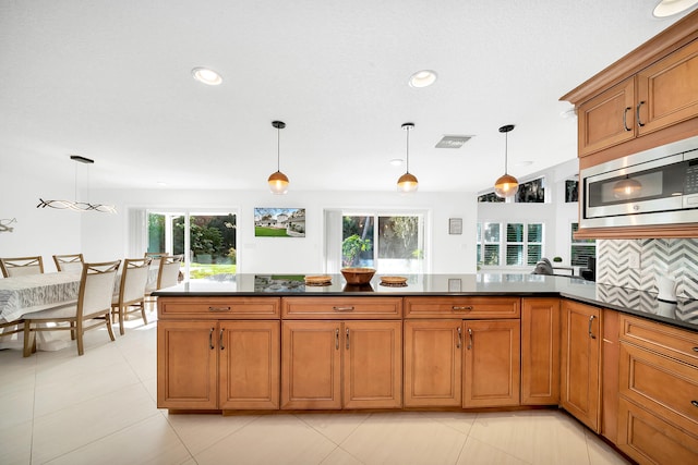 kitchen featuring stainless steel microwave, tasteful backsplash, and hanging light fixtures