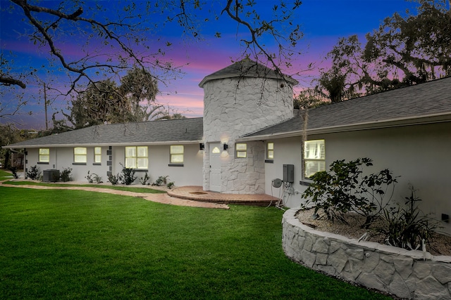 back house at dusk with cooling unit and a lawn