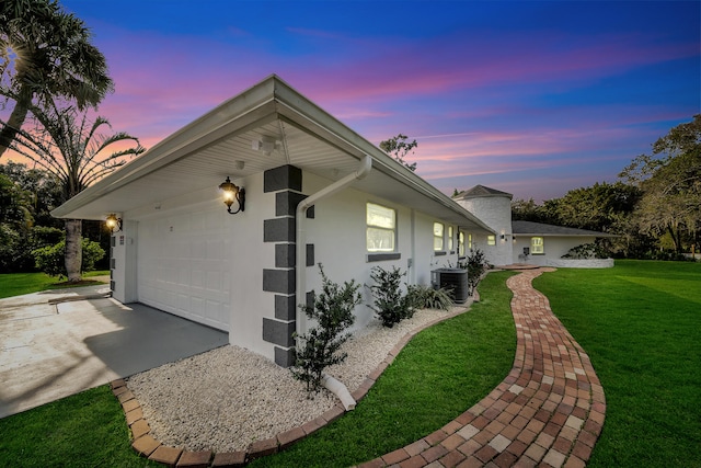 property exterior at dusk featuring a garage, central AC unit, and a yard