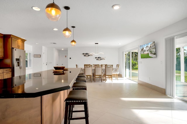 kitchen with light tile patterned floors, stainless steel fridge, a kitchen bar, and decorative light fixtures