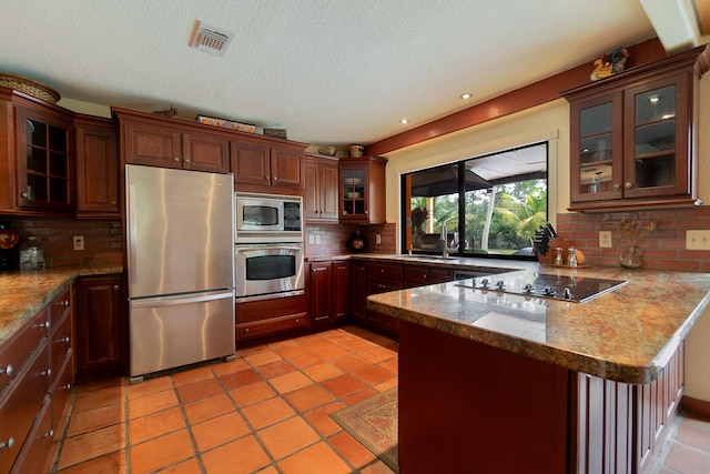 kitchen with visible vents, a sink, appliances with stainless steel finishes, a peninsula, and decorative backsplash