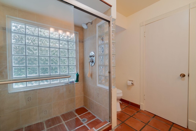 bathroom featuring tile patterned floors, toilet, a shower with shower door, and a wealth of natural light