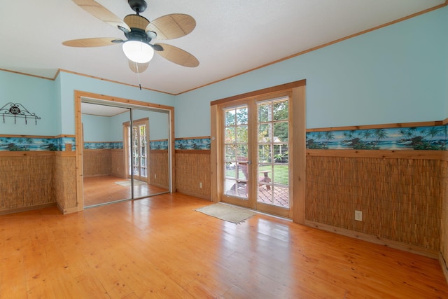 unfurnished room featuring a ceiling fan, crown molding, wood finished floors, and a wainscoted wall