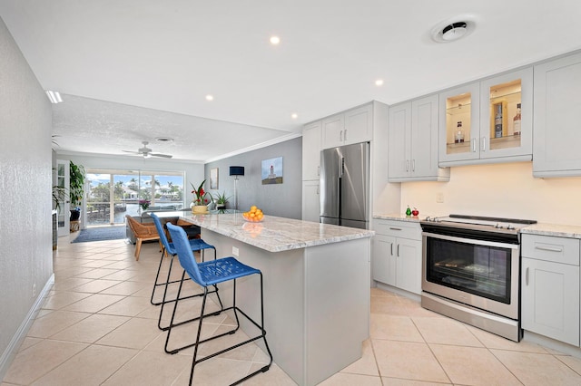 kitchen featuring light stone counters, a kitchen island, light tile patterned flooring, and appliances with stainless steel finishes