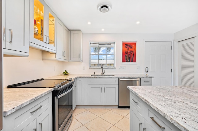 kitchen with sink, stainless steel appliances, light stone countertops, and light tile patterned flooring