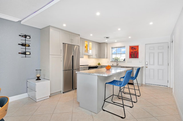 kitchen featuring light tile patterned flooring, appliances with stainless steel finishes, sink, a kitchen bar, and a center island