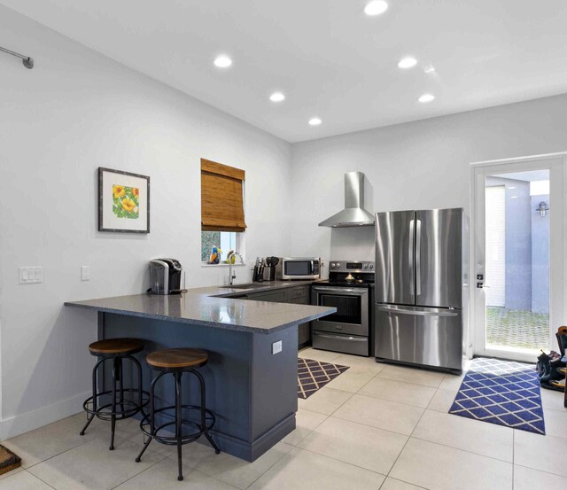 kitchen with a breakfast bar, kitchen peninsula, stainless steel appliances, wall chimney exhaust hood, and sink