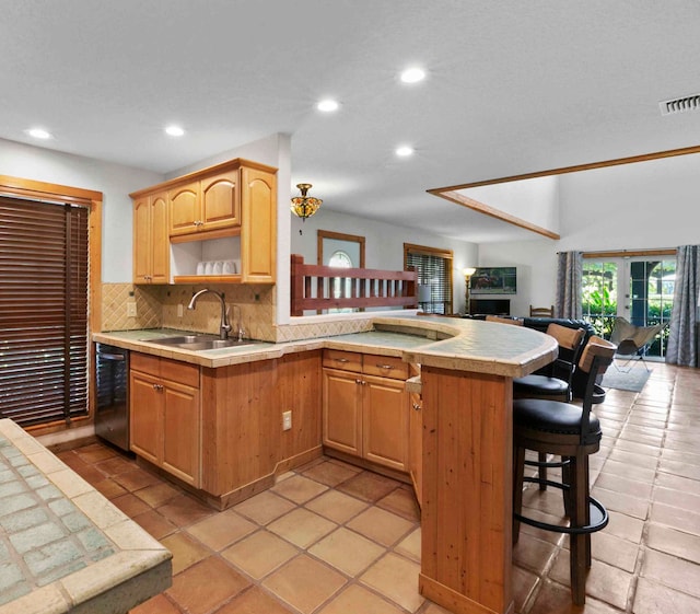 kitchen with light tile patterned flooring, tasteful backsplash, sink, black dishwasher, and a kitchen bar